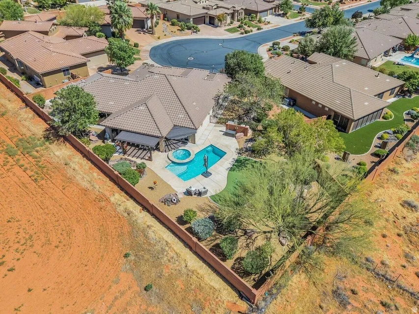 Resort-style backyard featuring a rectangular swimming pool with integrated spa, an expansive hardscaped pool deck, a covered patio with a pergola, and a xeriscaped landscape with mature trees