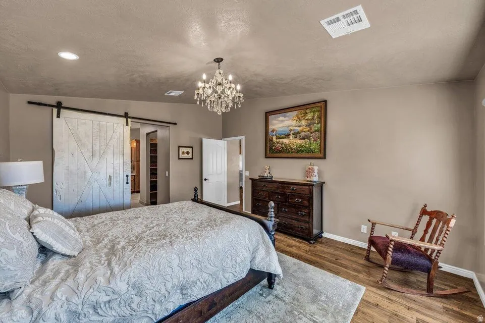 Wood-finish flooring, recessed lighting, and a crystal chandelier illuminate this space featuring a barn door entry to an additional area