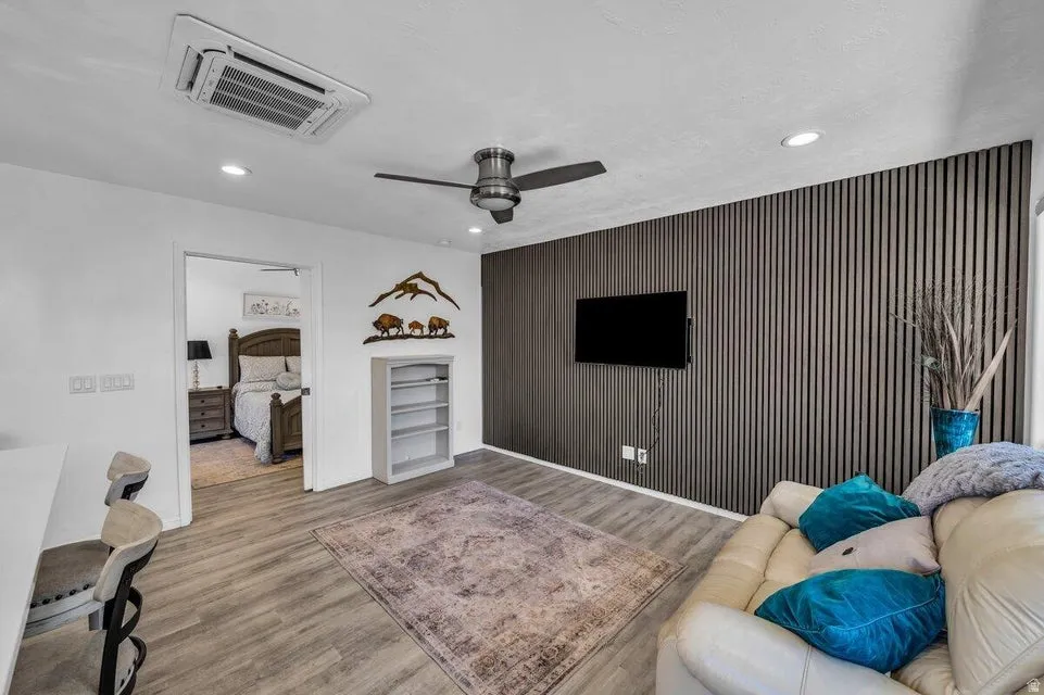 Living space featuring a textured accent wall, wood-finish flooring, recessed lighting, and a ceiling fan