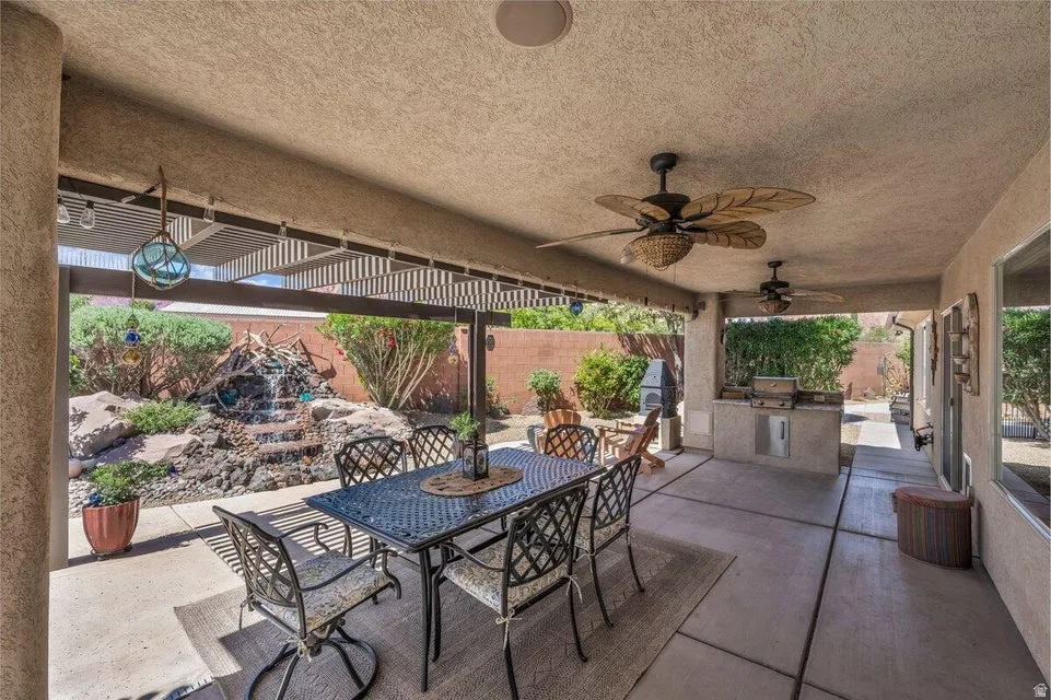 Covered patio featuring two ceiling fans, a built-in outdoor kitchen with grill, a rock water feature, and a partial lattice cover