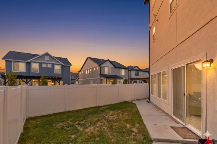 Private backyard with a concrete patio, perimeter fencing, and a manicured lawn area