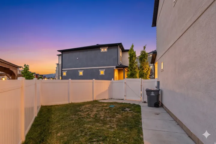 Private backyard space featuring a white vinyl fence, concrete pathway, and a grassy area