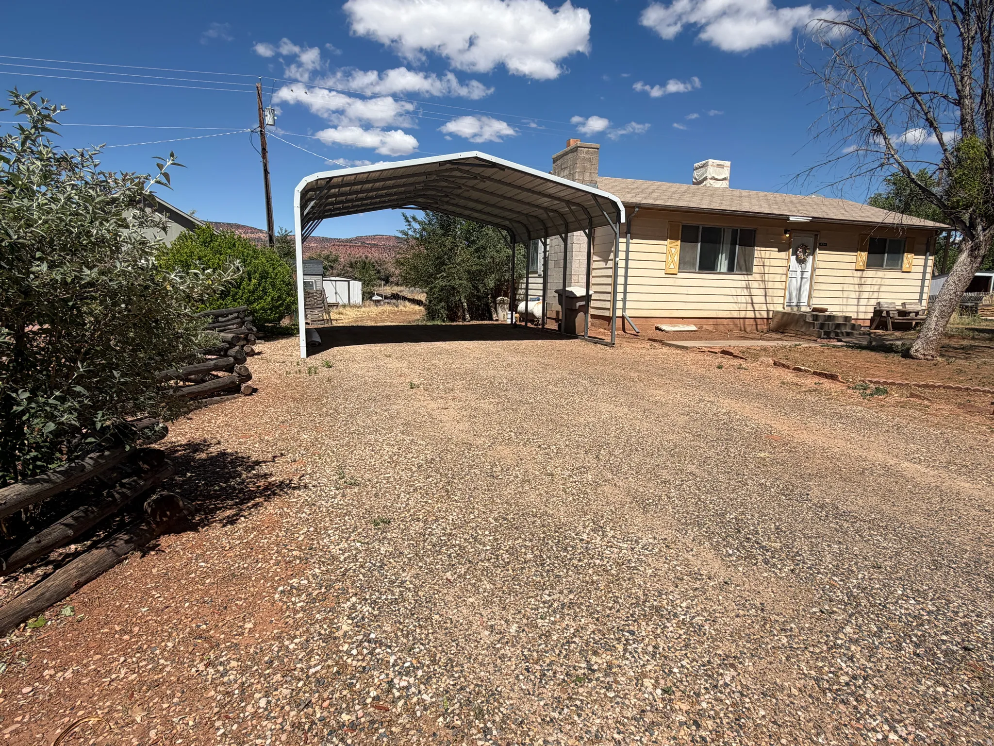 Single-story residence featuring light-colored siding, a covered carport, and a gravel driveway