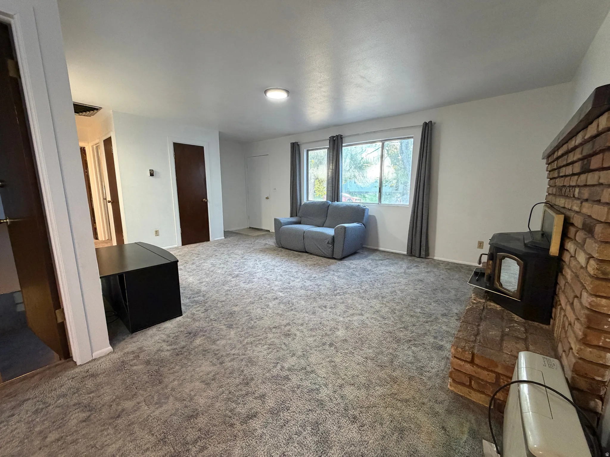Spacious living area featuring light-colored carpet flooring, white walls, and multiple windows providing natural light
