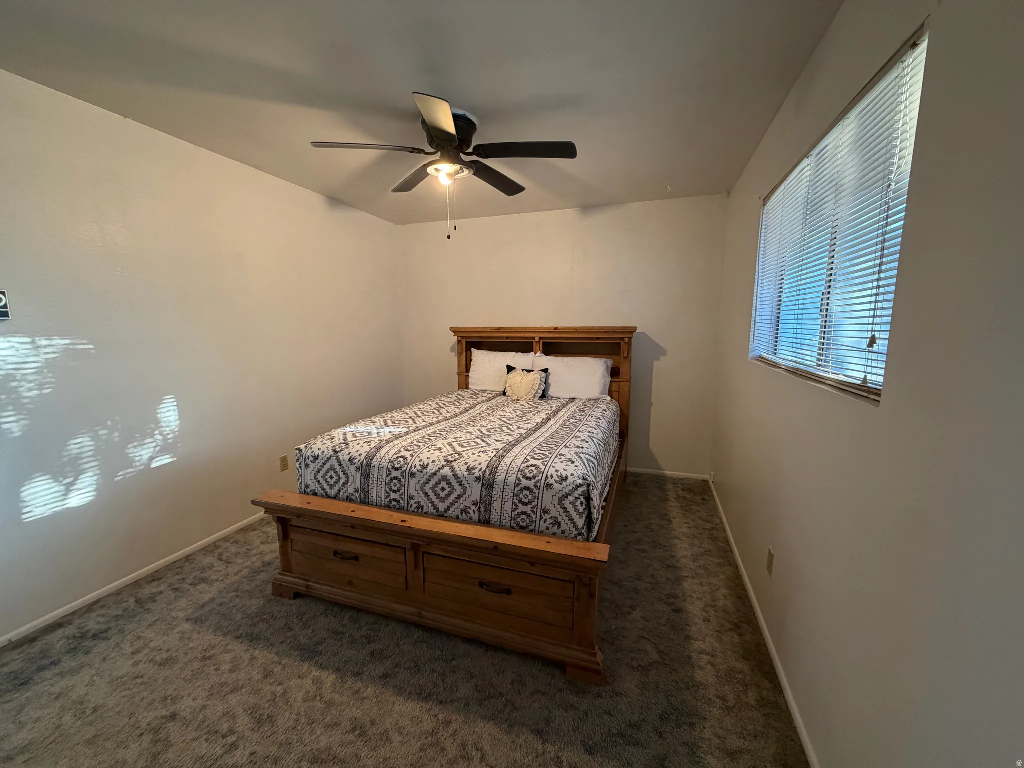 Room featuring neutral wall tones, textured carpeting, a window with blinds, and a ceiling fan with integrated lighting