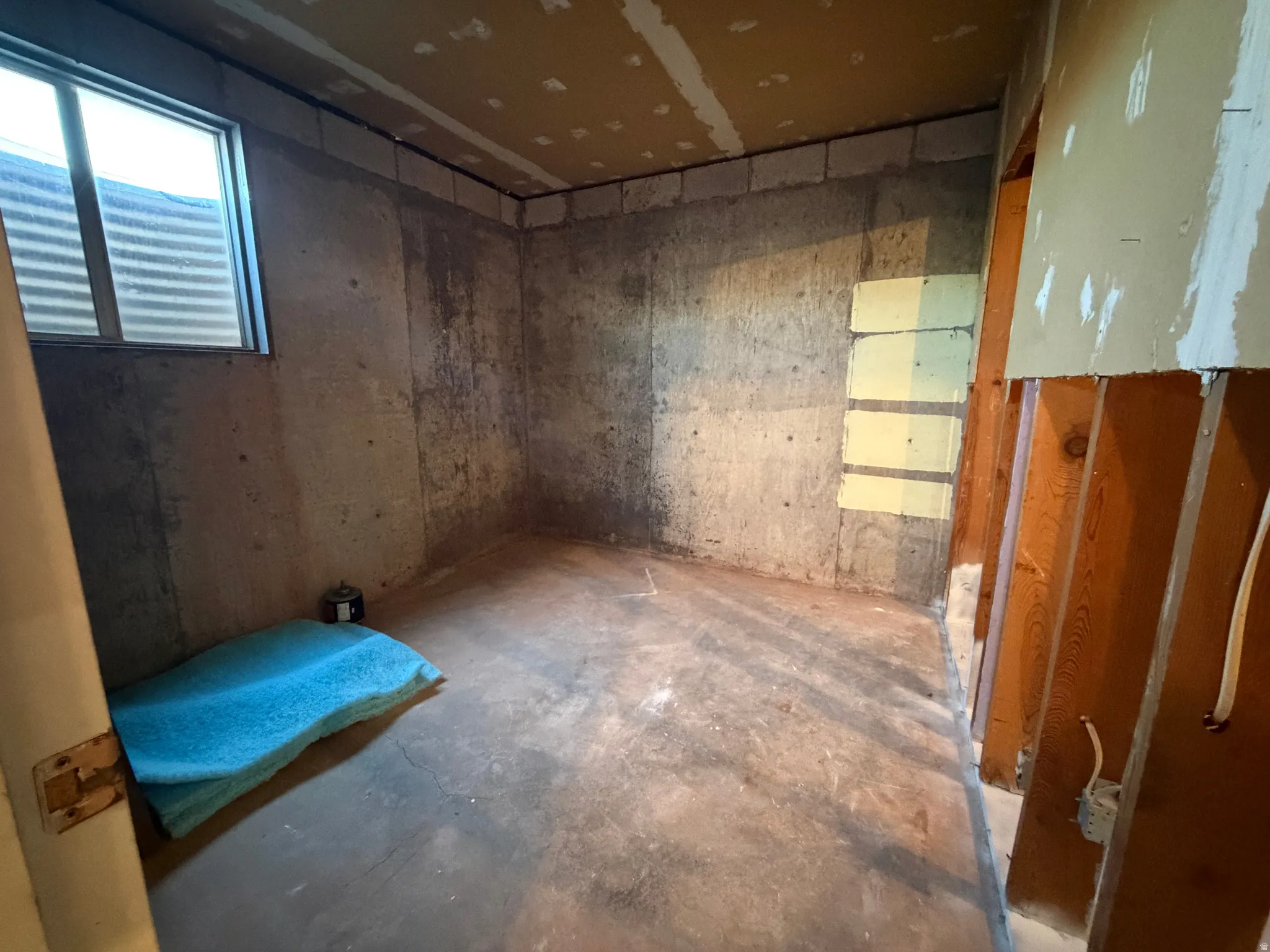 Concrete foundation walls featuring a small window with a window well