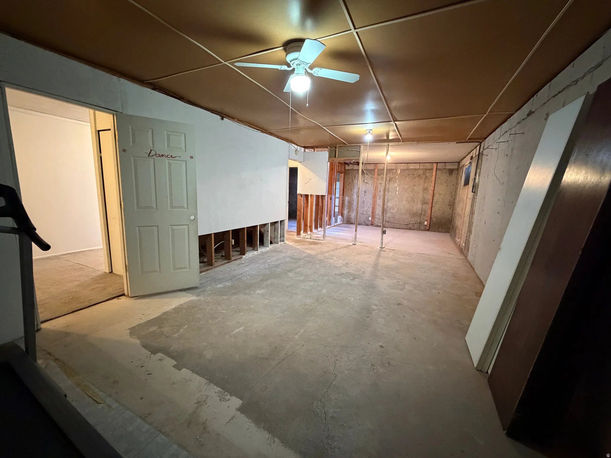 Unfinished basement space featuring exposed concrete flooring, suspended ceiling panels, and visible framing