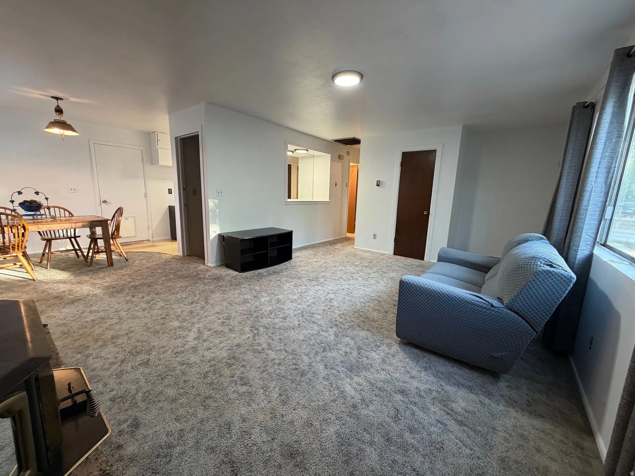 Open-concept living space featuring light gray carpeting, a built-in pass-through window, and a central ceiling light fixture