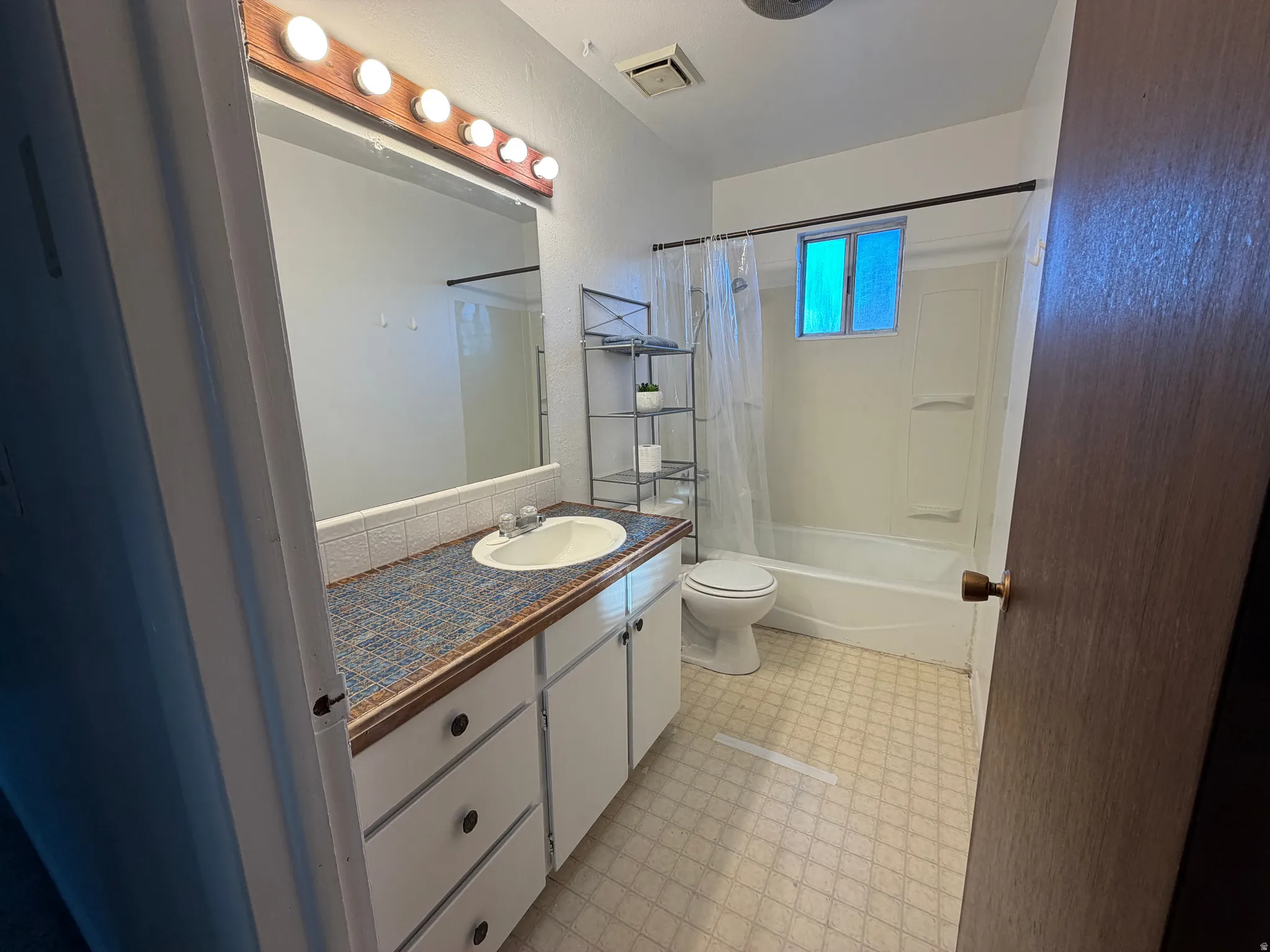 Bathroom vanity featuring a drop-in sink, patterned countertop, and wood-framed mirror with strip lighting