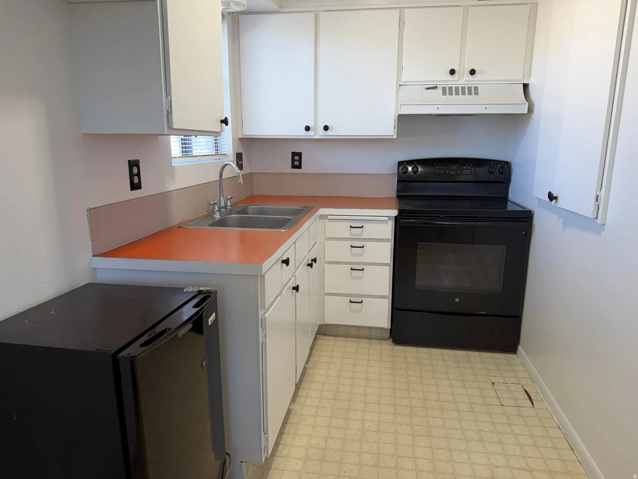 Kitchen featuring white cabinetry, orange countertops, a double-basin stainless steel sink, a black electric range, and patterned floor tiling