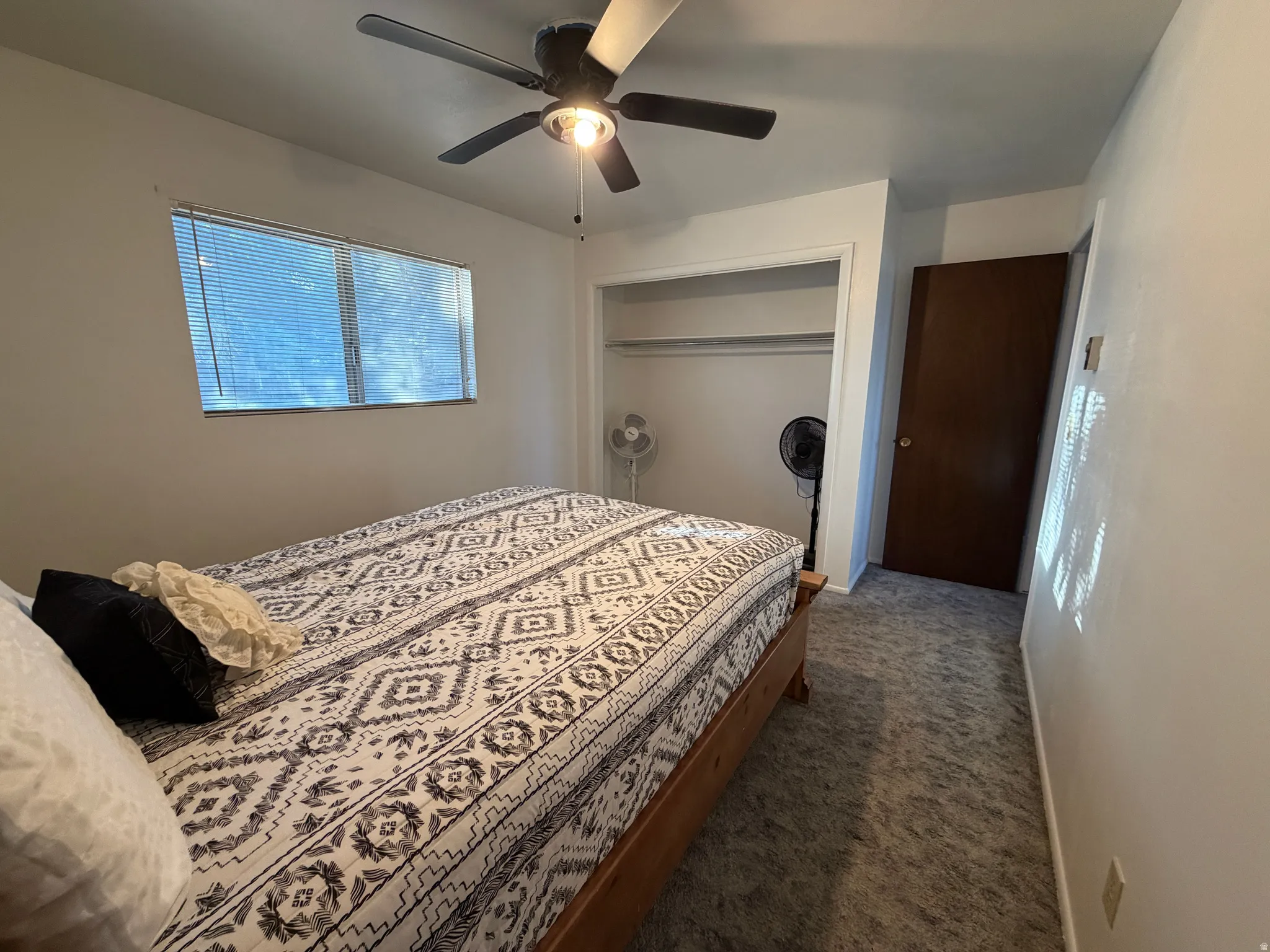Carpeted room featuring a ceiling fan with integrated lighting, a window with horizontal blinds, and an open closet with shelving