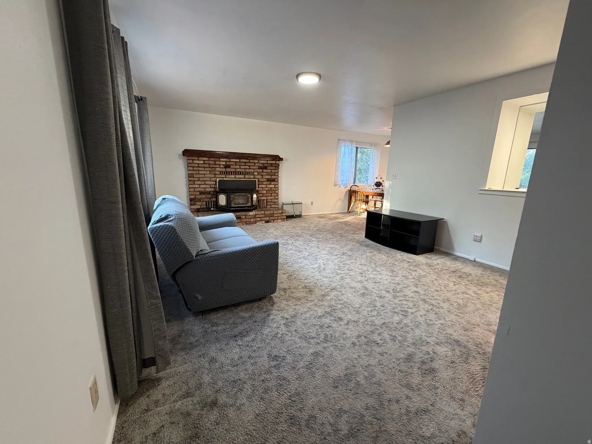 Spacious living area featuring soft carpet flooring, a prominent brick fireplace with a wood-burning insert, and a built-in window providing natural light