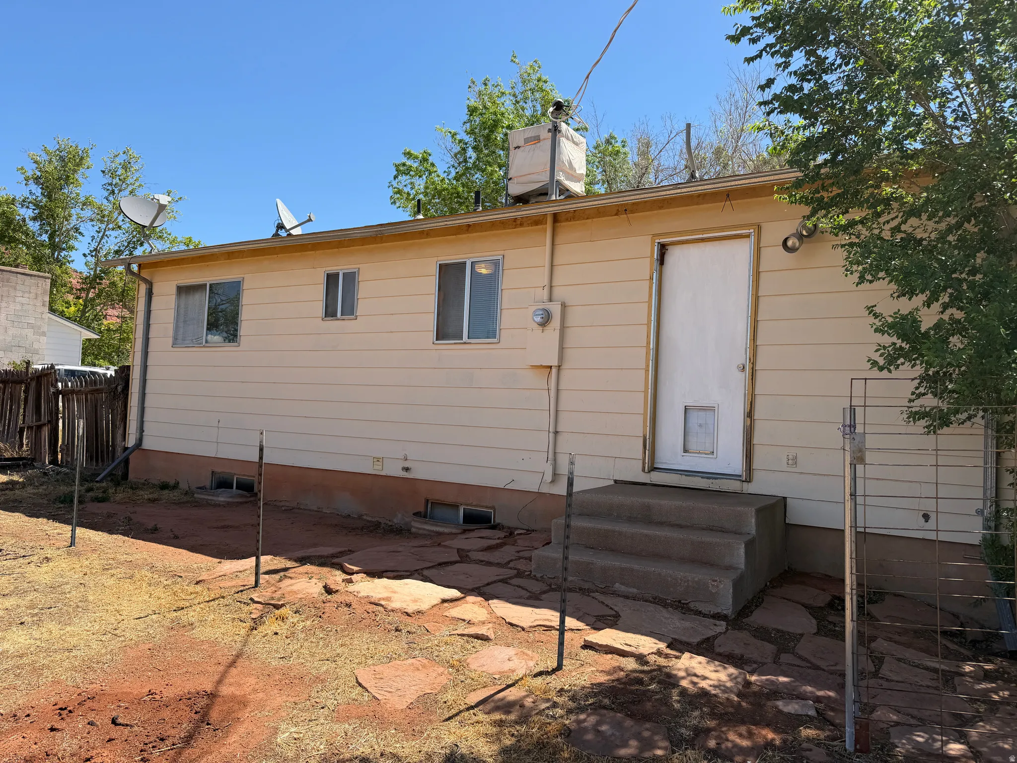 Rear exterior featuring beige horizontal siding, a white entry door with a pet door, and three windows