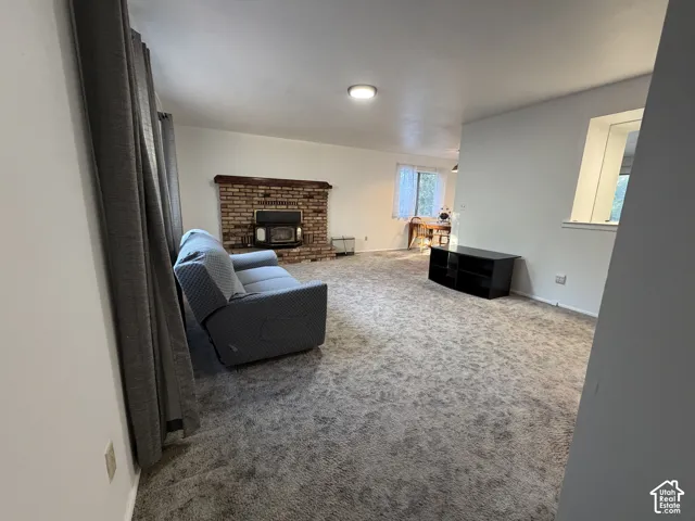 Spacious living area featuring soft carpet flooring, a prominent brick fireplace with a wood-burning insert, and a built-in window providing natural light