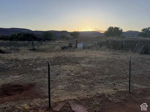 Backyard at evening time.  Expansive outdoor space featuring natural landscaping, distant mountainous terrain, and visible fencing elements