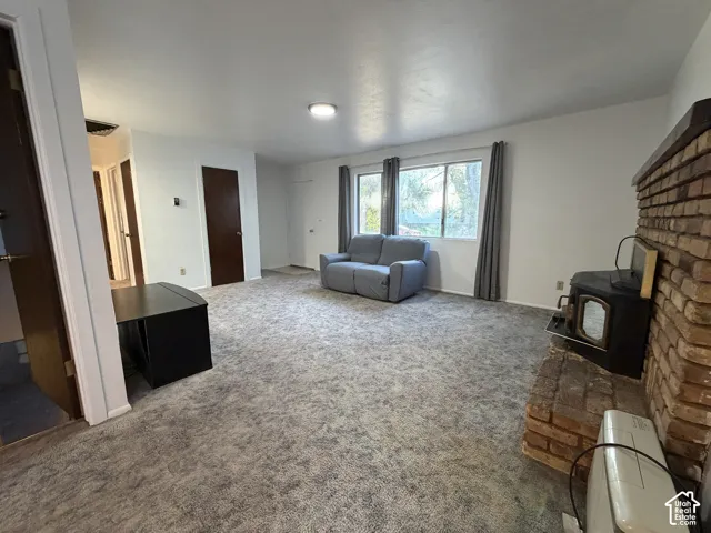 Spacious living area featuring light-colored carpet flooring, white walls, and multiple windows providing natural light