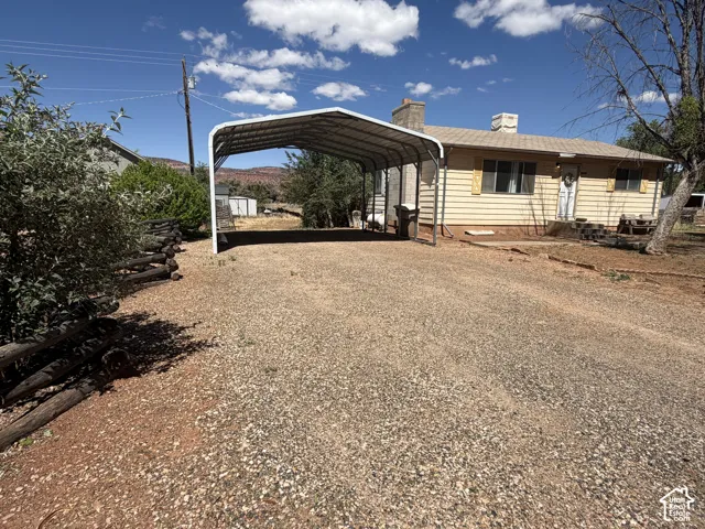 Single-story residence featuring light-colored siding, a covered carport, and a gravel driveway