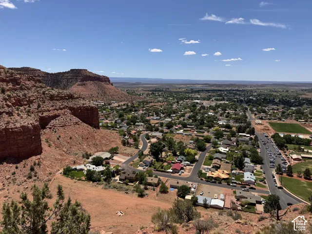 Expansive aerial capturing a community featuring residential properties, mature green landscaping, and paved roadways, set against a backdrop of natural red rock formations and distant open terrain