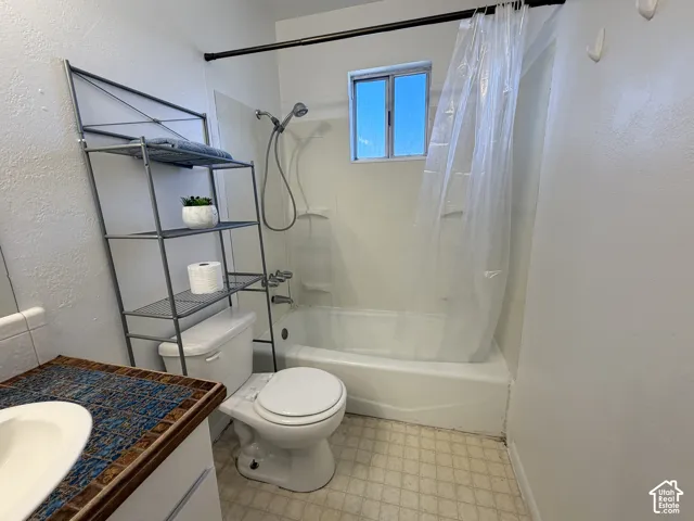Bathroom featuring a white bathtub with an integrated shower, a window, and a vanity with a patterned tile countertop and integrated sink