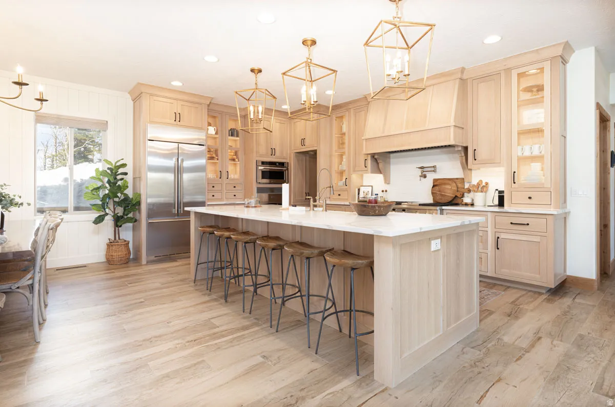 Spacious kitchen featuring light wood cabinetry, a large center island with a stone countertop, stainless steel appliances, and integrated range hood