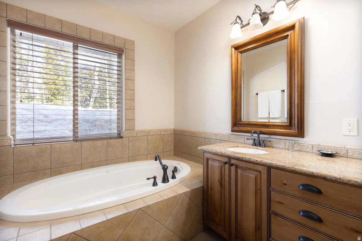 Soaking tub surrounded by tile, featuring a window with wooden blinds