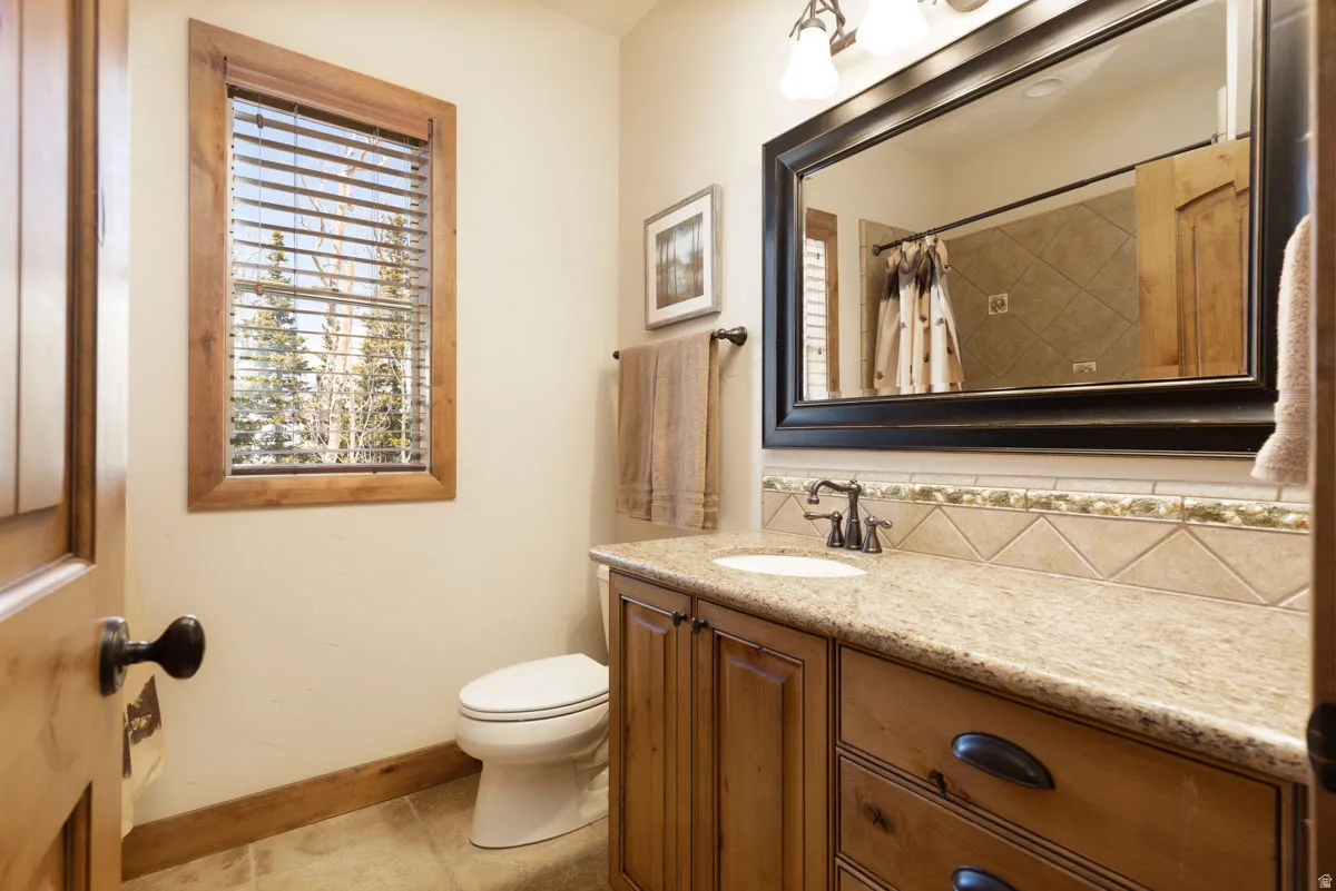 Bathroom featuring a wood-framed window, natural wood vanity with stone countertop, drop-in sink, and a large framed mirror