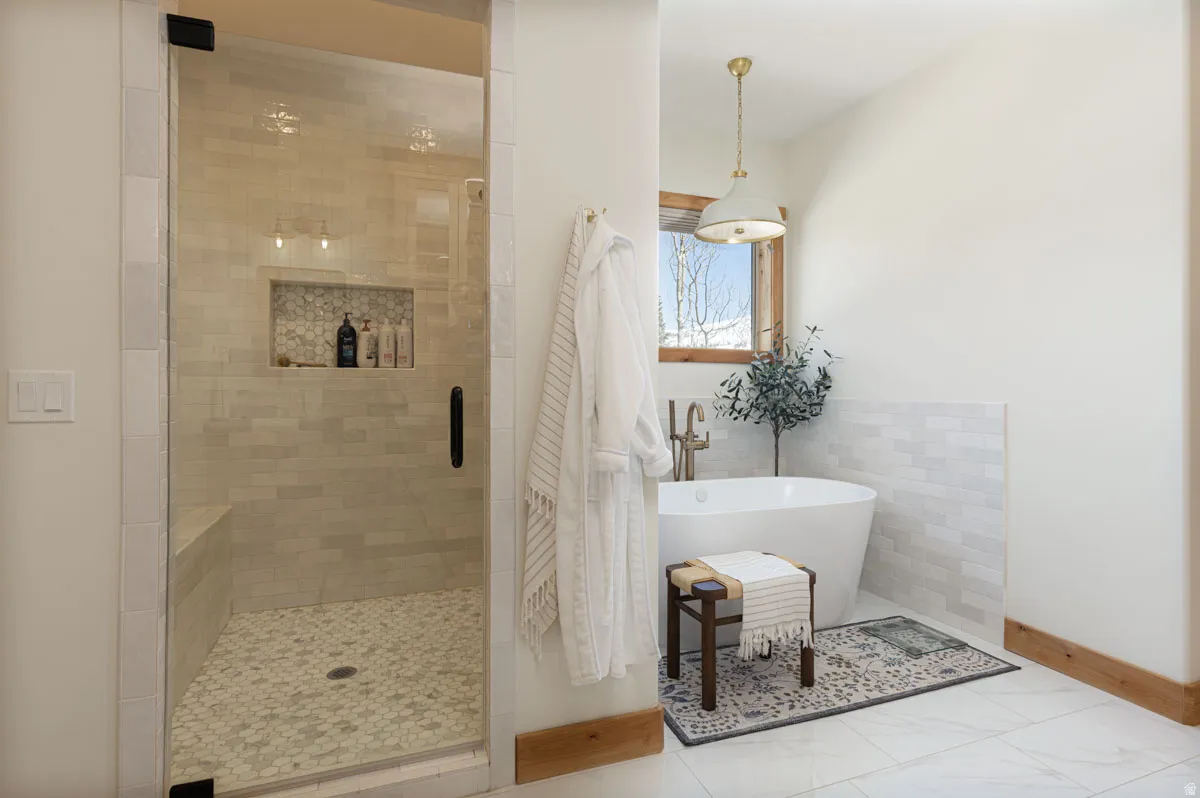 Freestanding soaking tub with brushed brass fixtures, complemented by a large walk-in shower featuring a built-in bench, glass enclosure, and mosaic tile flooring