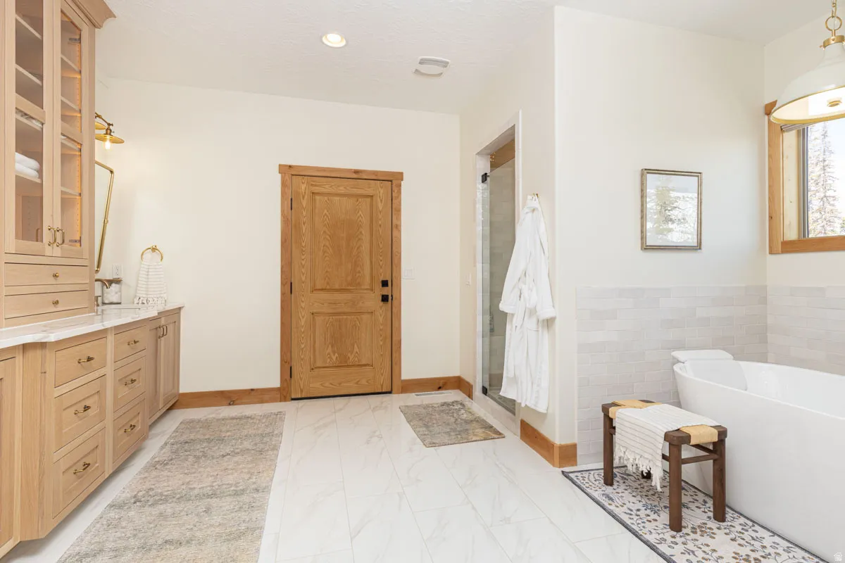 Bathroom featuring a floating double vanity with a marble-finish countertop, a freestanding soaking tub, a glass-enclosed shower, wood-finish flooring, and natural wood trim accents