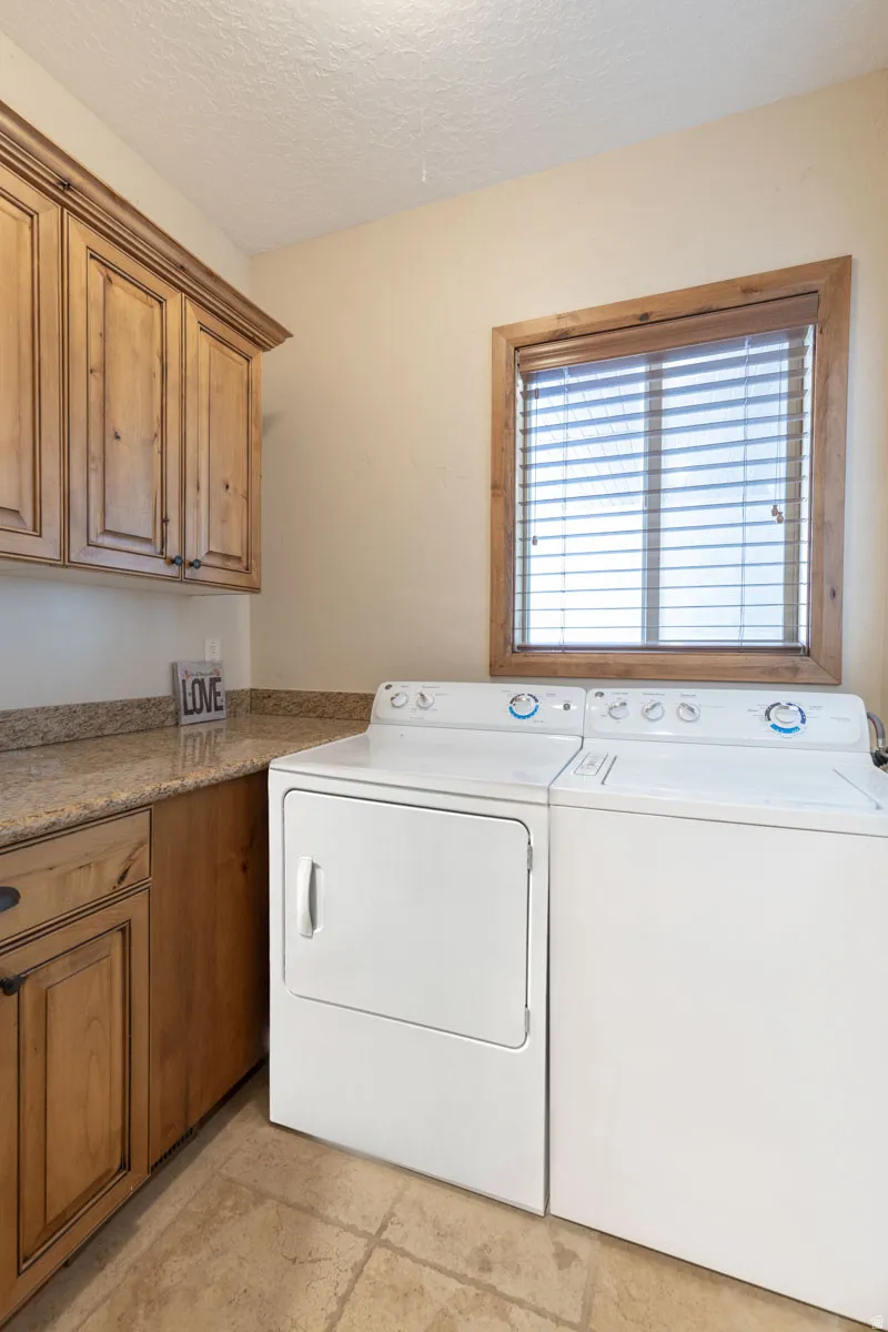 Laundry area featuring wood-finish cabinetry with dark hardware, a stone-finish countertop, and tiled flooring
