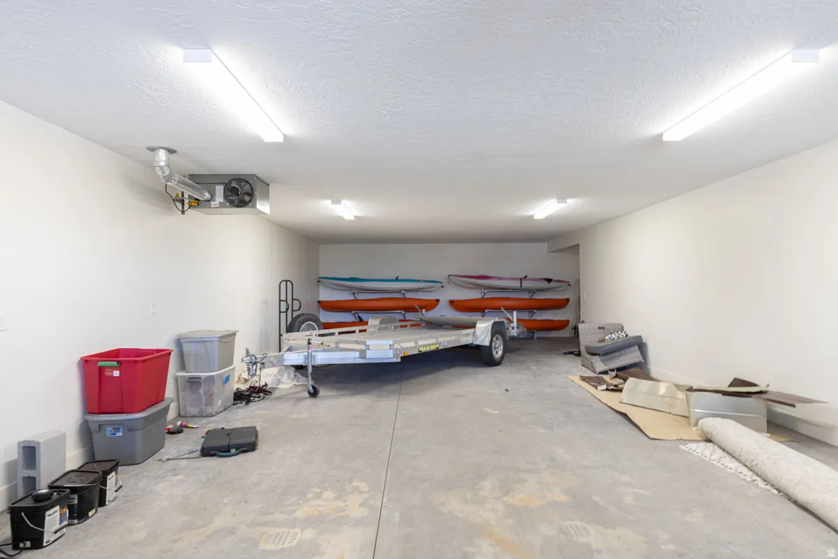 Spacious garage featuring a concrete floor, multiple ceiling-mounted fluorescent lights, white painted walls, and an exposed ventilation unit
