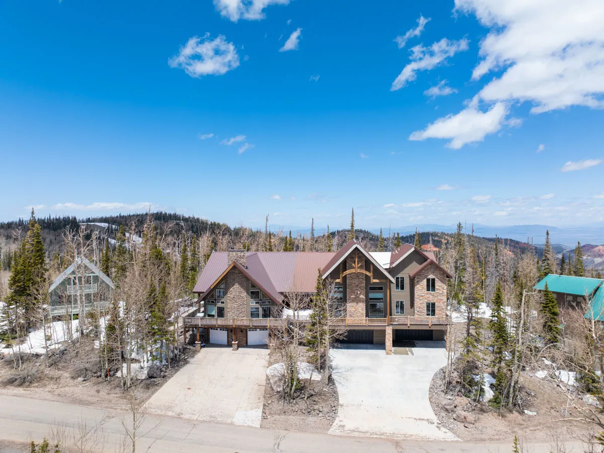 Stone and stucco multi-level residence with a multi-gabled metal roof, elevated deck, and a multi-car garage