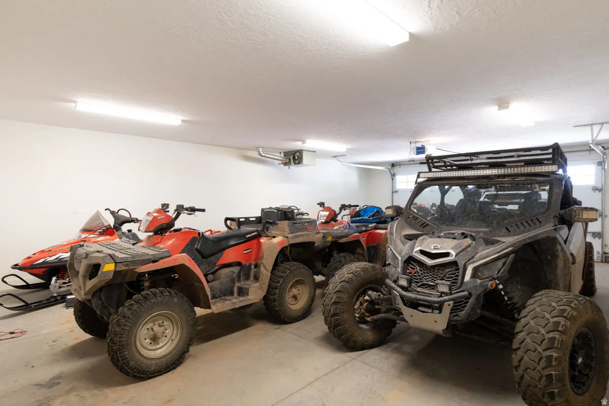 Spacious garage featuring a concrete floor, white walls, multiple fluorescent light fixtures, and a roll-up garage door with window inserts