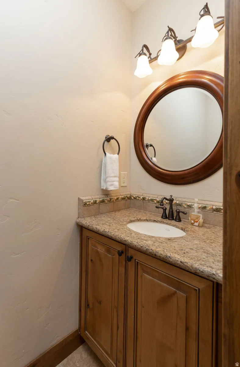 Bathroom vanity featuring a light-toned countertop, wood-finish cabinetry, an oval mirror with a wood frame, and a three-light fixture