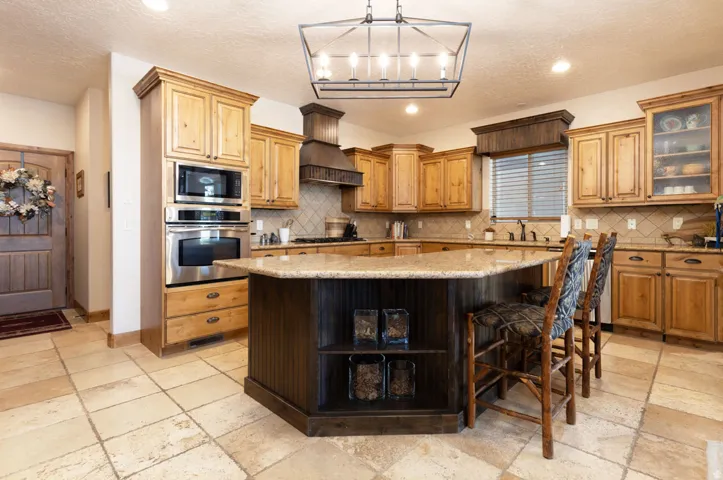 Spacious kitchen featuring an angled island with a granite countertop, light wood cabinetry, stainless steel double ovens, and tile flooring