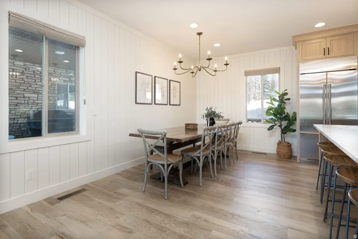 Dining area featuring plank-style wood-finish flooring, white shiplap wall paneling, a bronze chandelier, recessed lighting, and a window with a roller shade