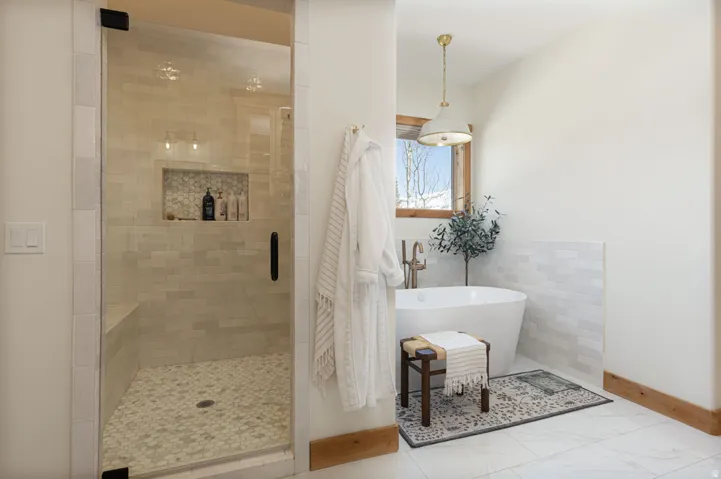 Freestanding soaking tub with brushed brass fixtures, complemented by a large walk-in shower featuring a built-in bench, glass enclosure, and mosaic tile flooring