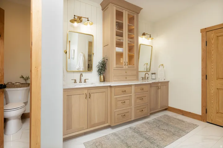 Dual vanity with light wood-finish cabinetry, white countertops, and brushed brass hardware