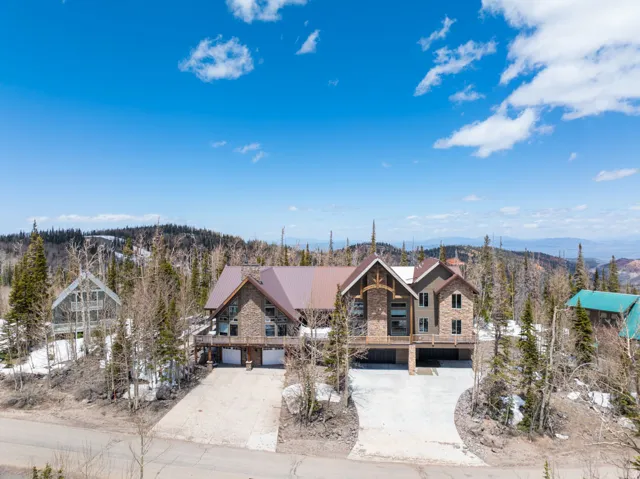 Stone and stucco multi-level residence with a multi-gabled metal roof, elevated deck, and a multi-car garage