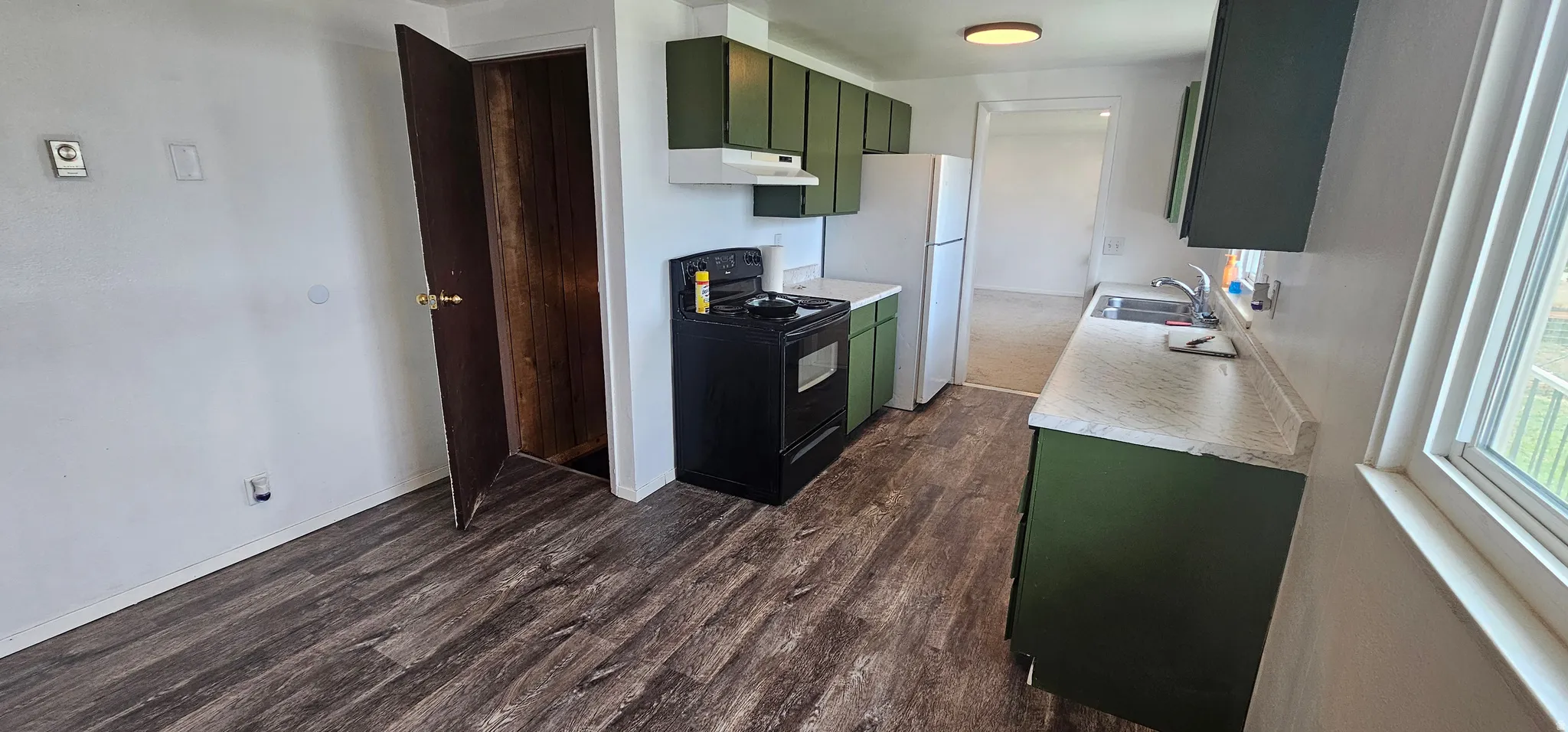 Kitchen featuring wood-finish flooring, green cabinetry, a black range, and white countertops