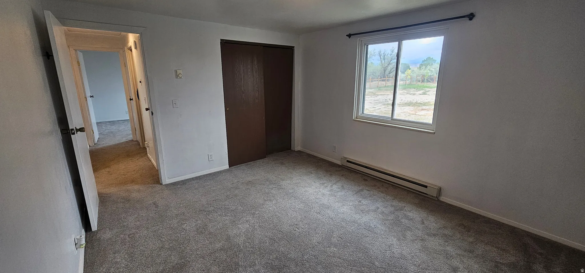 Bedroom featuring gray carpet, a double window with a dark curtain rod, a baseboard heating unit, and a dark wood-finish sliding closet door