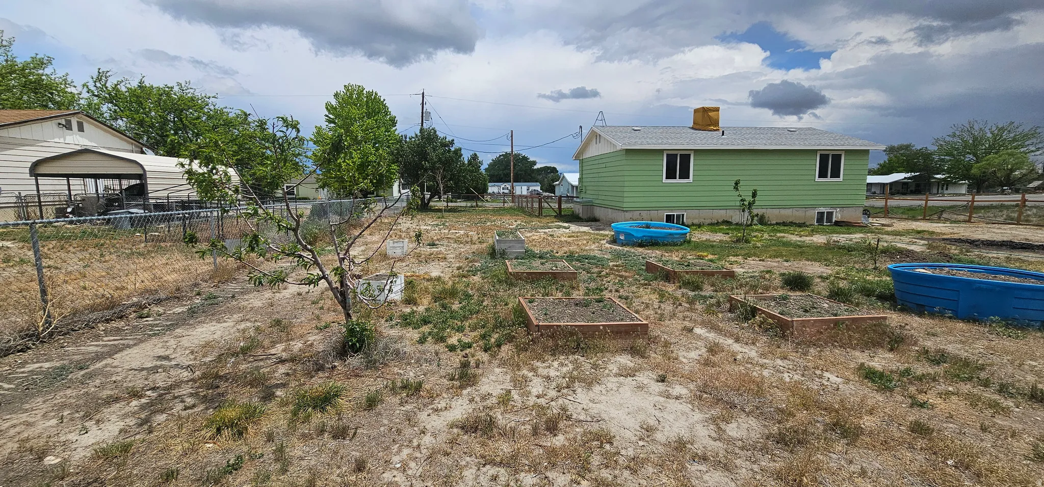 Expansive backyard featuring multiple raised garden beds and a chain-link fence