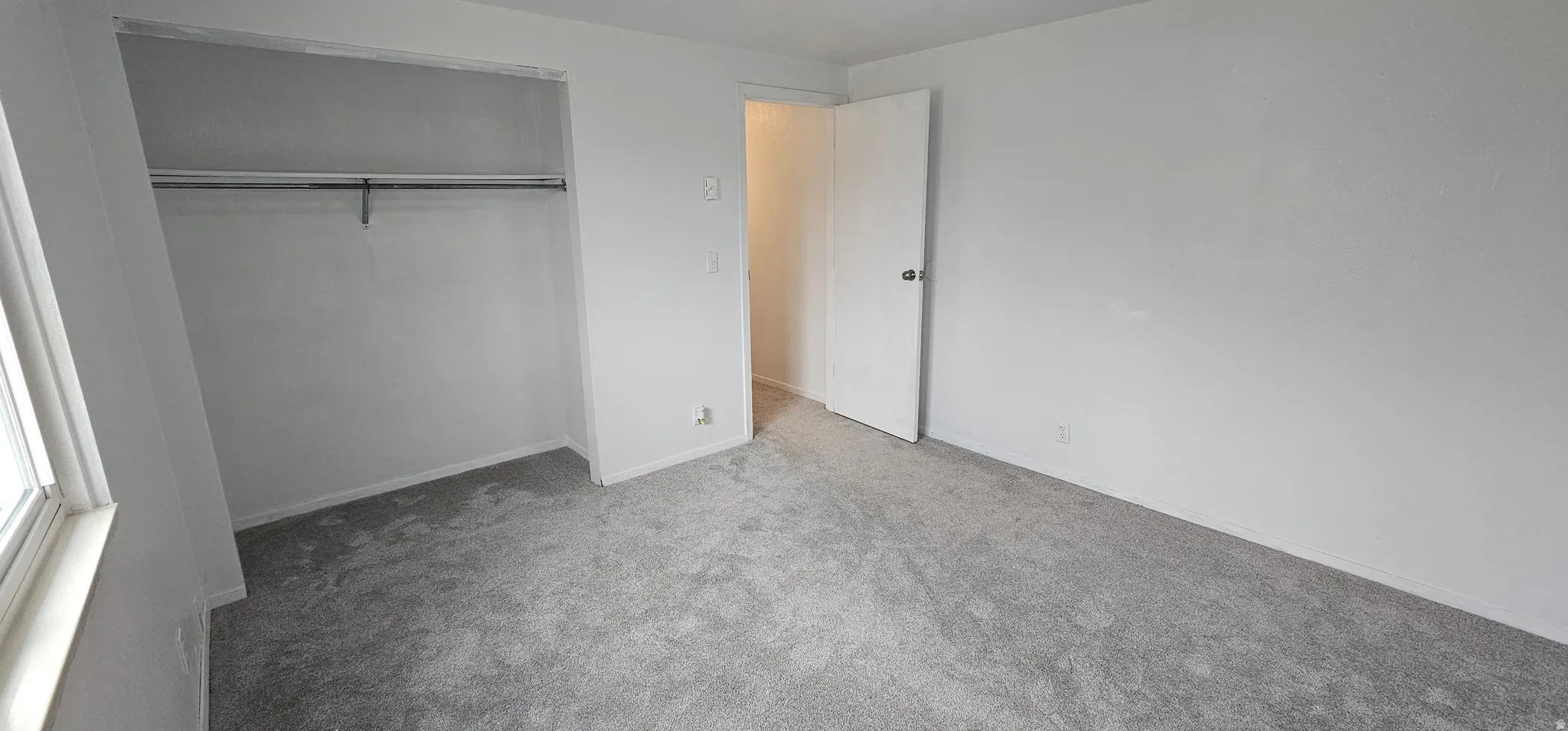 Room featuring light gray carpeting, white painted walls, a window with natural light, and a built-in closet with a hanging rod