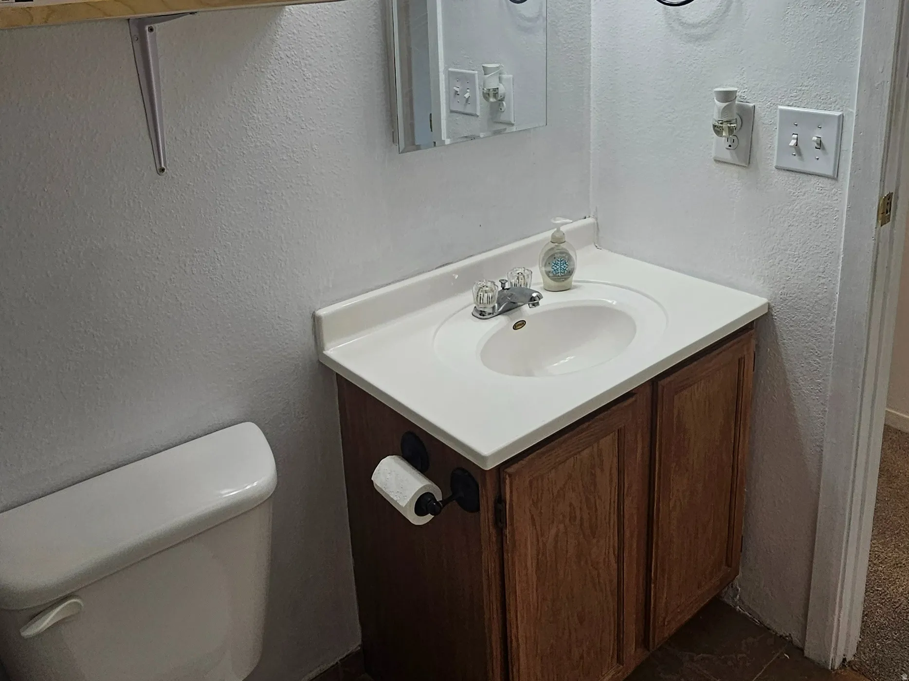 Bathroom featuring a wood-finish vanity with a white countertop and integrated sink, a mirrored medicine cabinet, a three-light vanity fixture, and brown tile flooring