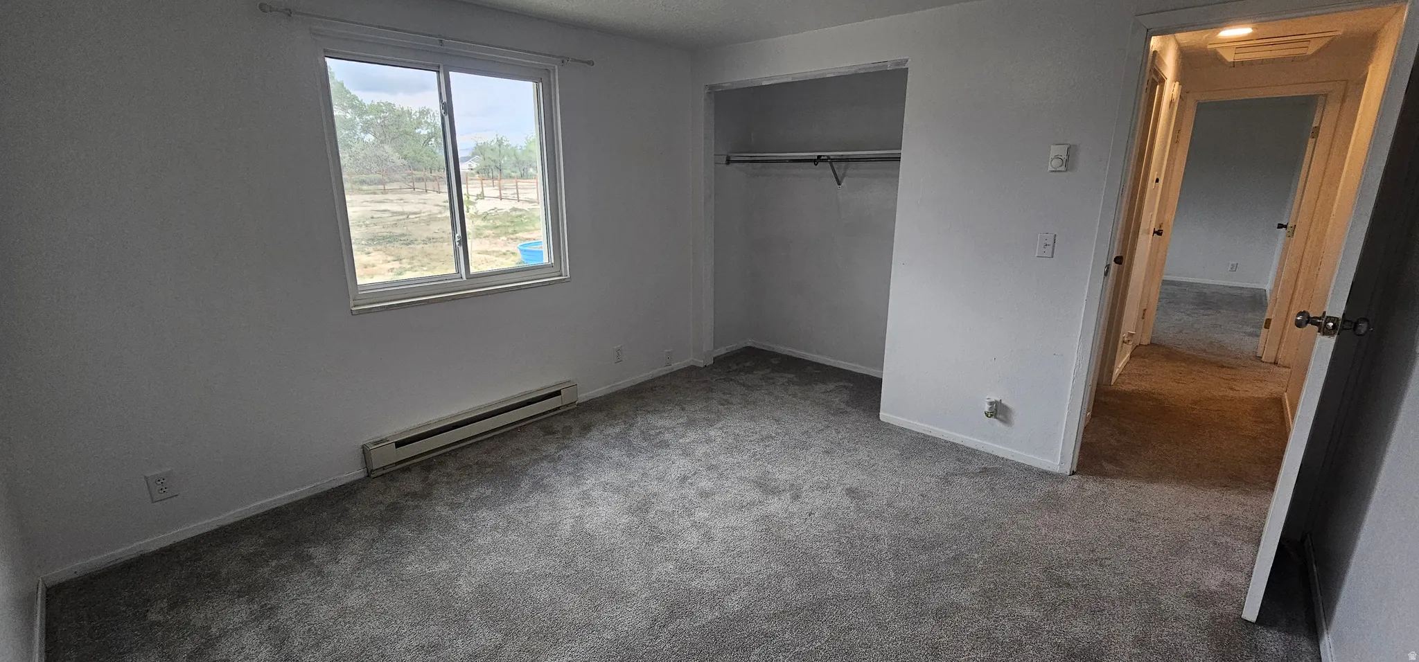Carpeted interior space featuring a window, baseboard heating unit, and an open closet with a hanging rod