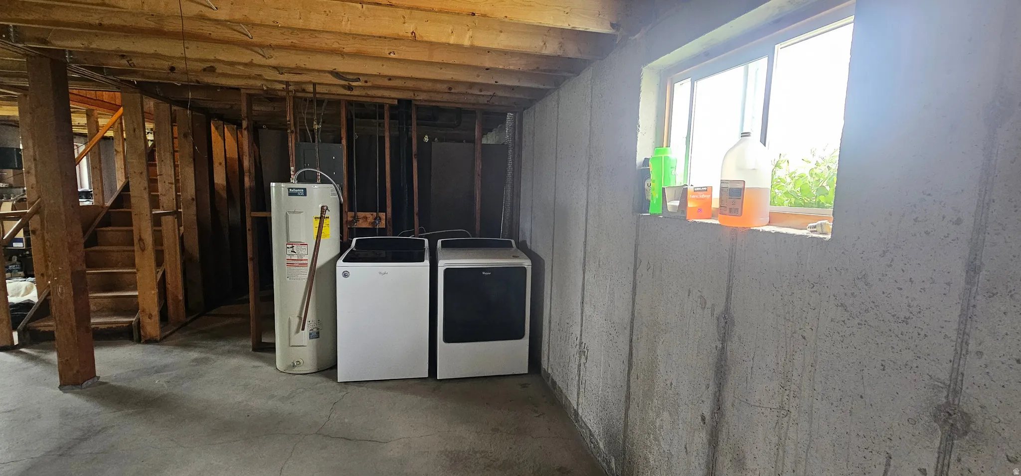 Unfinished basement featuring exposed wood joists, a concrete floor, and a water heater