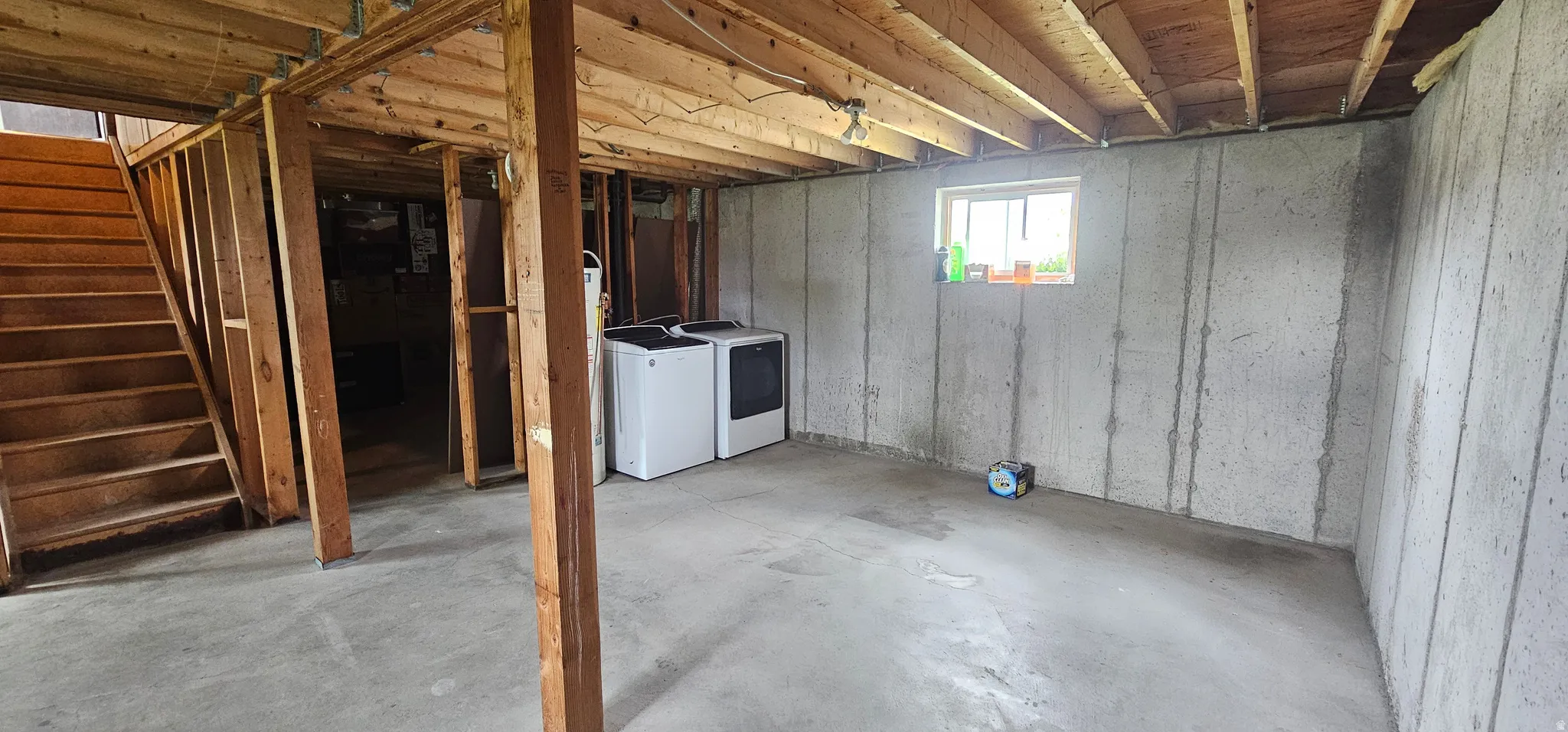 Unfinished lower level featuring concrete flooring, exposed wood beam ceiling, framed walls, and a window providing natural light
