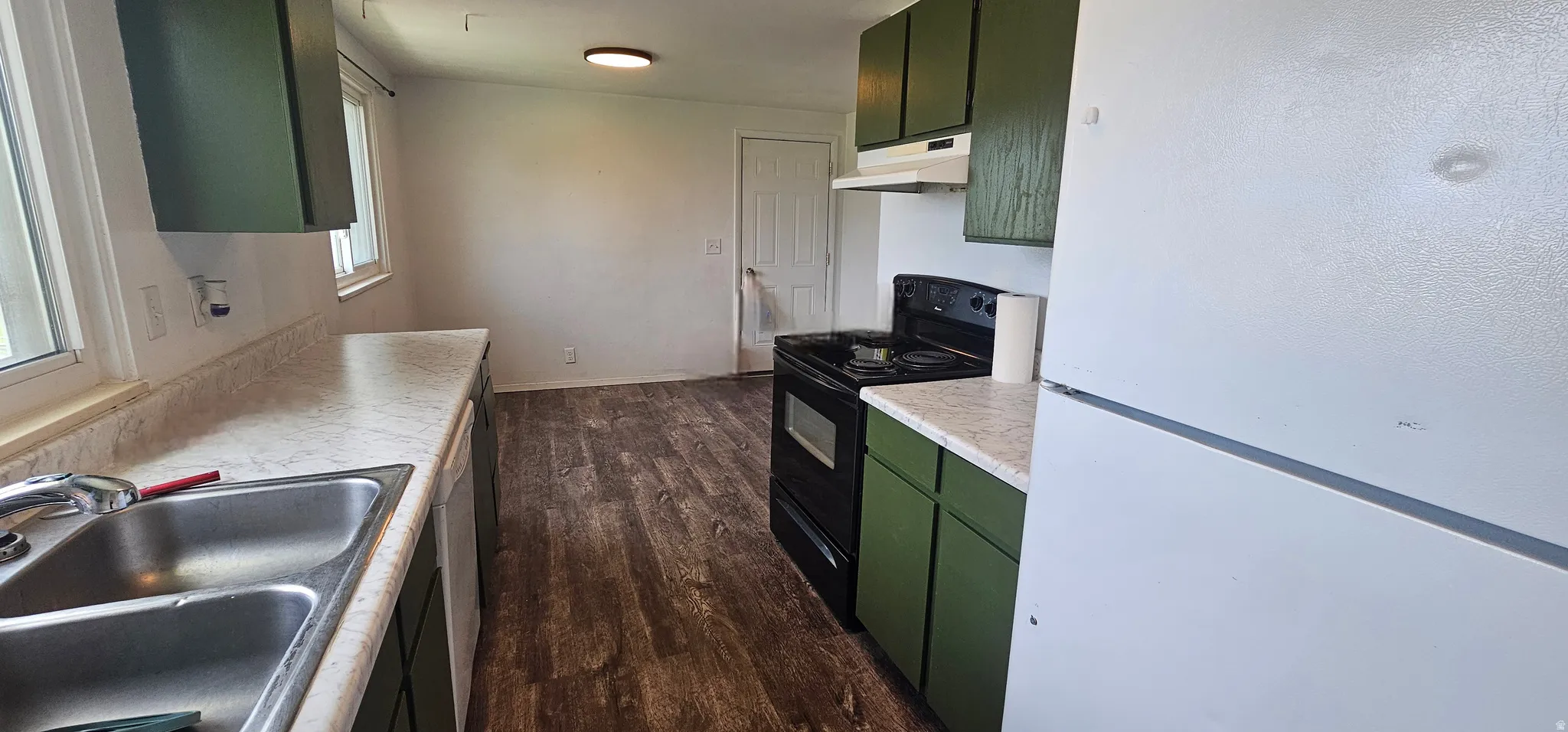 Kitchen featuring wood-finish flooring, green cabinetry, white countertops, and white appliances