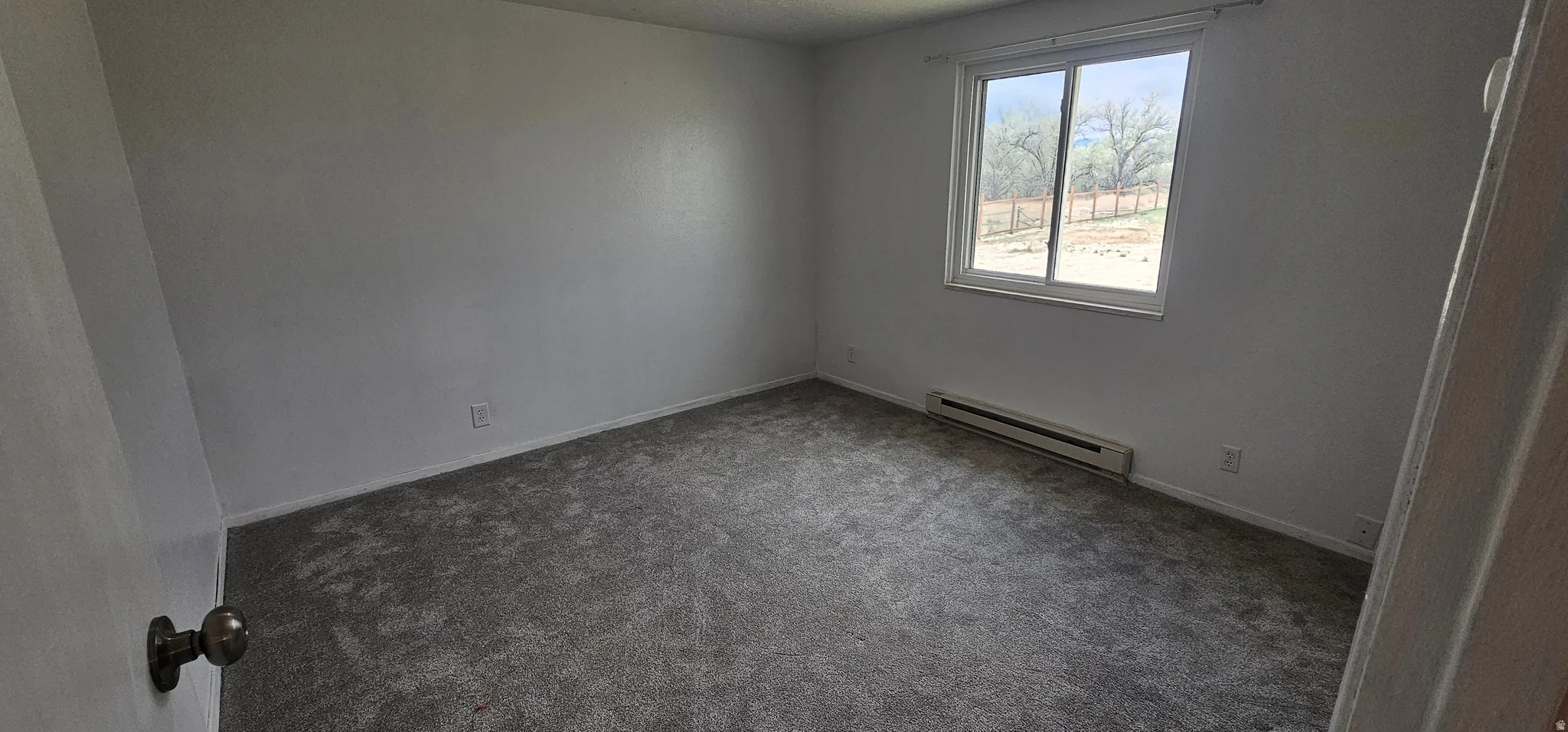 Carpeted room with a large window, baseboard heating unit, and neutral wall tones