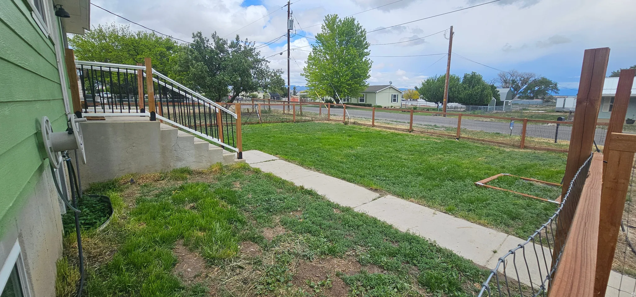 Expansive yard featuring a concrete walkway, wood and wire fencing, and mature trees