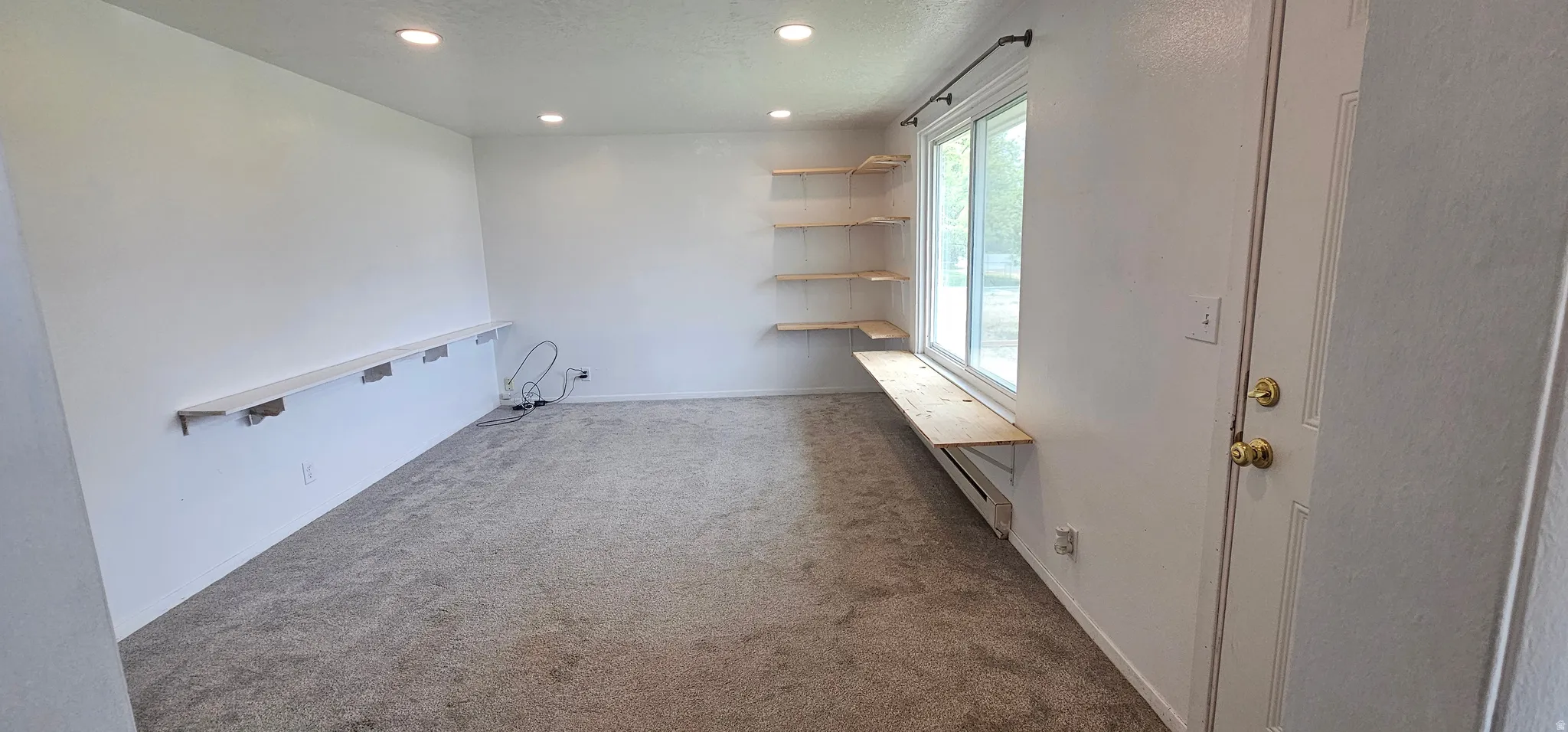 Carpeted room featuring recessed lighting, a wide window, built-in shelving, and a desk-height surface extending along the window